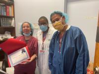 Three people in hospital garb, one holds certificate